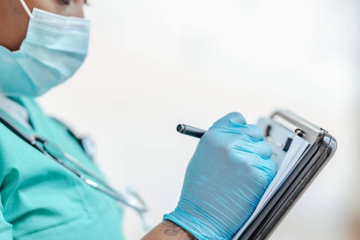 A pediatric clinician in teal scrubs with a stethoscope, reviewing notes on a clipboard.